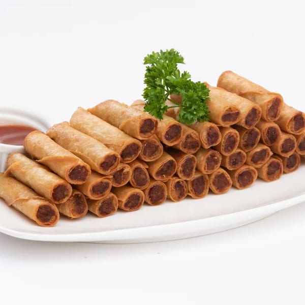 A large plate of Goldilocks' crispy Filipino lumpia rolls with a side of dipping sauce.