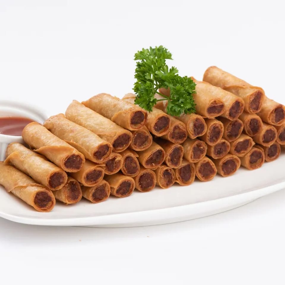 A large plate of Goldilocks' crispy Filipino lumpia rolls with a side of dipping sauce.