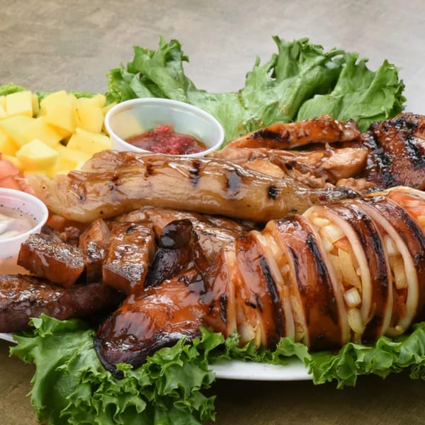 Grilled squid, chicken, and pork with mangoes, lettuce, and dipping sauces on a white plate.