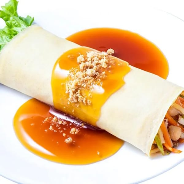 Filipino fresh lumpia with sweet sauce and crushed peanuts on a white plate.