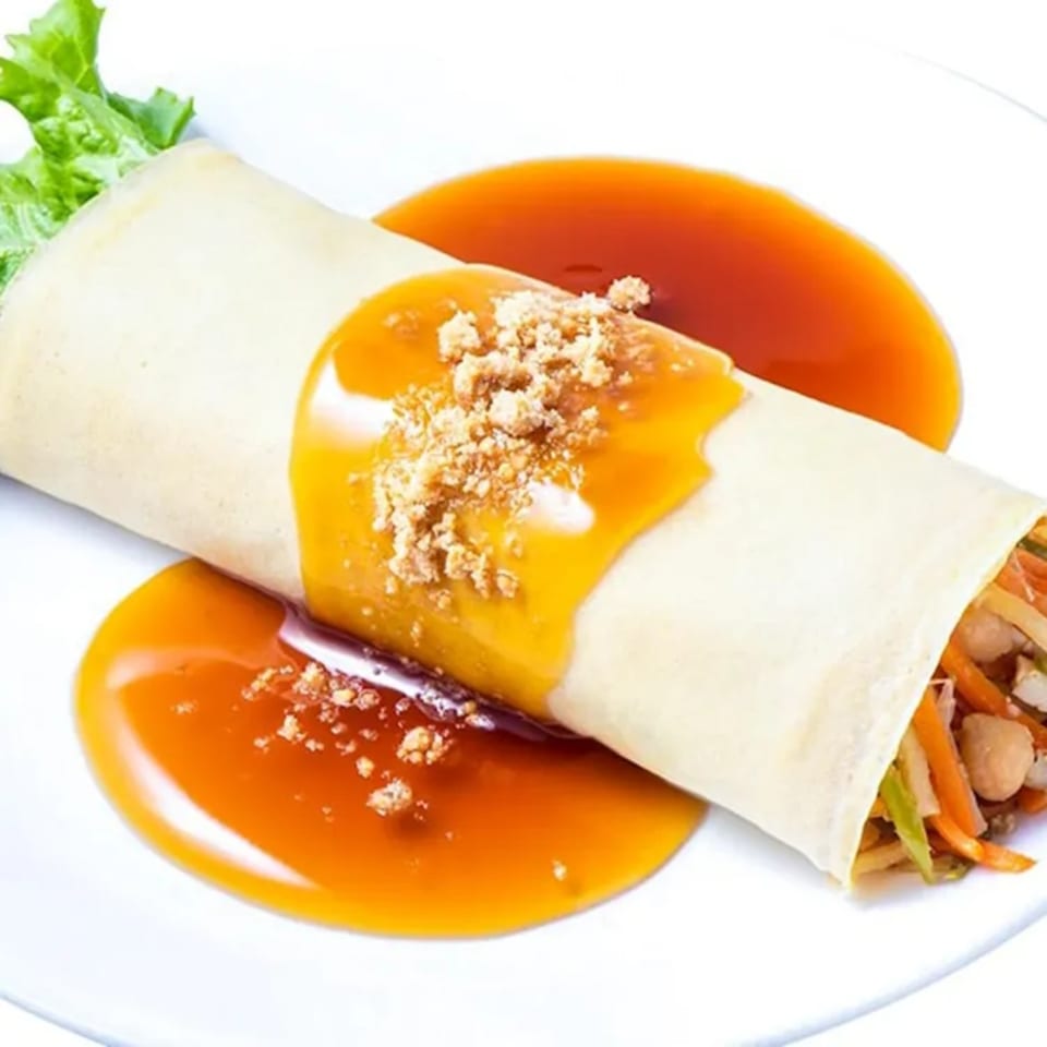 Filipino fresh lumpia with sweet sauce and crushed peanuts on a white plate.