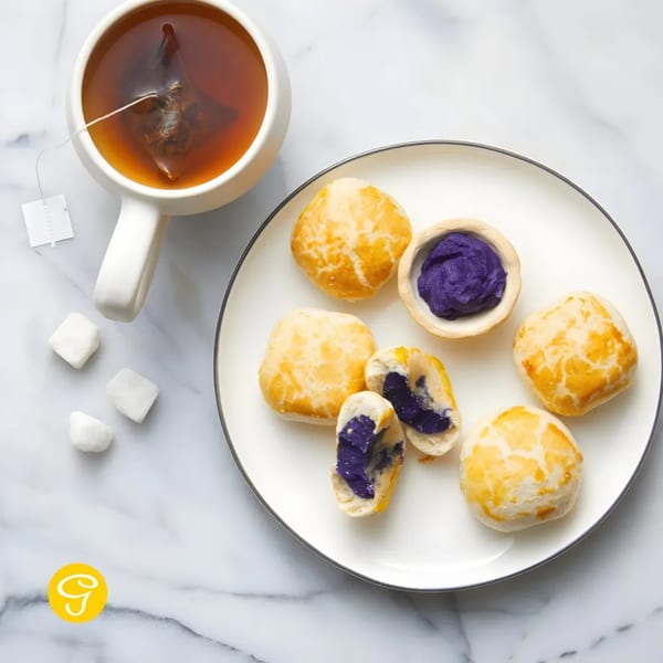 Goldilocks ube ensaymada pastries and a cup of tea with sugar cubes on a marble surface.