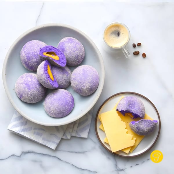 Purple ube pandesal with yellow cheese filling, coffee, and coffee beans on a marble surface.